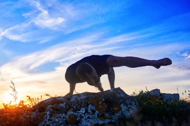 Çekici bir adam gecenin gündoğumu karşı kayaya yoga yaparken.
