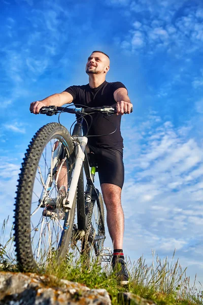 Нижний вид улыбающегося велосипедиста с велосипедом на фоне голубого неба с облаками . — стоковое фото