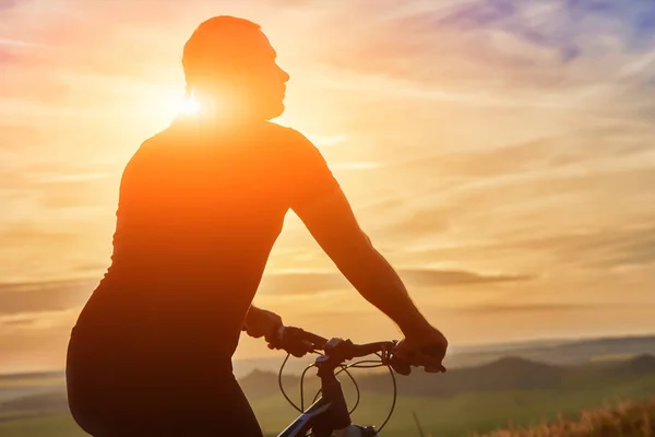Крупный план силуэта велосипедиста, стоящего с велосипедом на фоне красивого заката . — стоковое фото