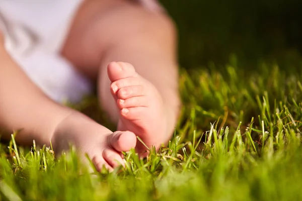 Pequeños pies de bebé en la hierba verde en verano día soleado en el parque . — Foto de Stock