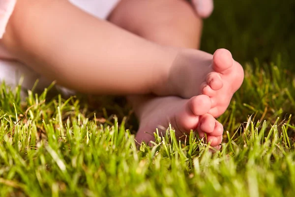 Pequeños pies de bebé en la hierba verde en verano día soleado en el parque . — Foto de Stock