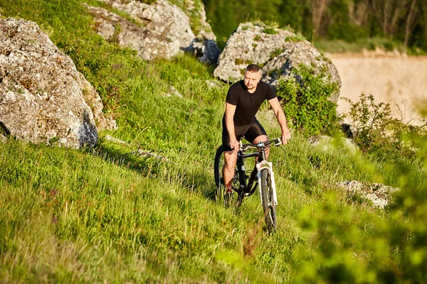 Atractivo ciclista montando la bicicleta en el sendero de verano cerca de hermosas rocas grandes . — Foto de Stock