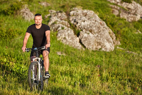 Ciclista atraente andando de bicicleta na trilha de verão perto de belas rochas grandes . — Fotografia de Stock