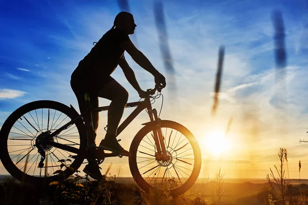 Silhueta de um ciclista com uma bicicleta no fundo do céu em belo pôr do sol . — Fotografia de Stock