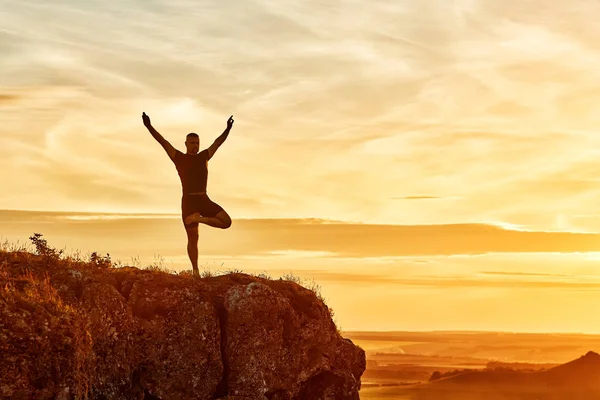 Pratik yoga güzel gün batımını karşı tepedeki adam silüeti. — Stok fotoğraf