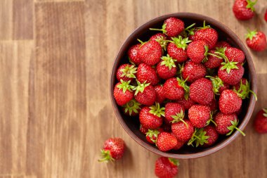 Ahşap masa üzerinde bir kahverengi kil kase taze kırmızı çilek.