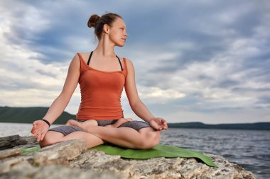 Çekici kadın güzel Nehri yakınında taş yoga uygulamak.