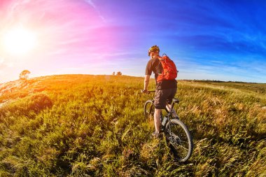 Genç bisikletçi binme dağ Bisiklet güzel gökyüzü karşı yeşil çayır aracılığıyla.