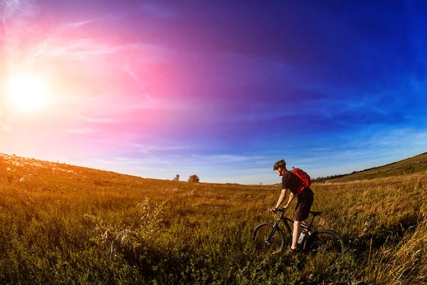 Junge Radfahrerin fährt mit Mountainbike durch grüne Wiese gegen schönen Himmel. — Stockfoto