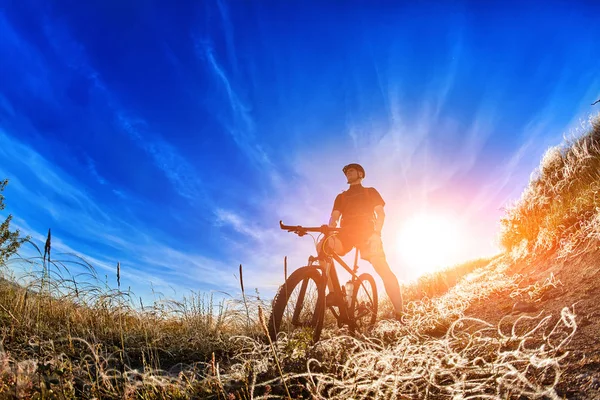 Вид з низьким кутом на велосипедиста, що стоїть з гірським велосипедом на схід сонця . — стокове фото