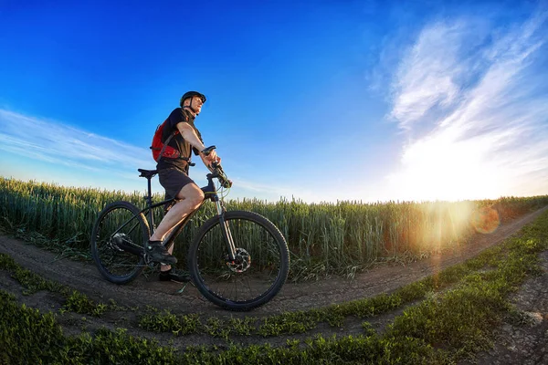 Vidvinkel på cyklisten stående på spåret på fältet mot vackra landskap. — Stockfoto