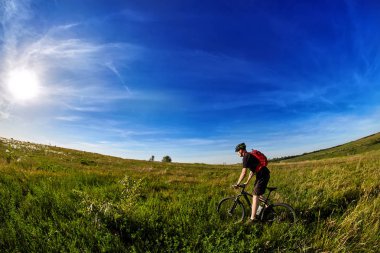 Genç bisikletçi binme dağ Bisiklet güzel gökyüzü karşı yeşil çayır aracılığıyla.