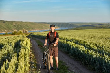 Genç çekici bisikletçi dağ bisikletçi yaz yeşil alanı ile ayakta.