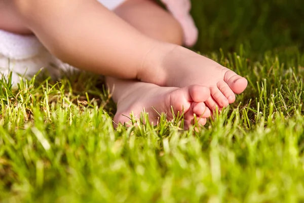 Primer plano de las pequeñas piernas de bebé sobre una hierba verde en el parque de la ciudad . — Foto de Stock