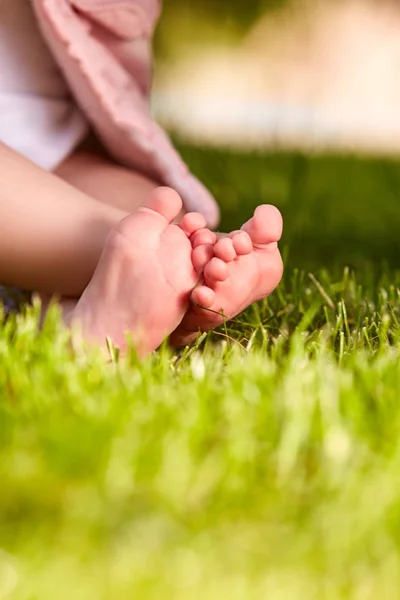 Primer plano de las pequeñas piernas de bebé sobre una hierba verde en el parque de la ciudad . — Foto de Stock