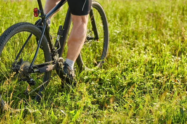 Közeli kép a kerékpáros férfi lábát, mountain bike lovaglás a zöld rét. — Stock Fotó