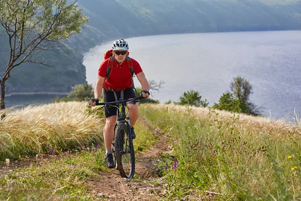 Mladý cyklista na kole v zelené letní louky proti krásné krajině. — Stock fotografie