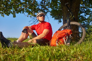Kırsal kesimde döngüsü yakınındaki çayır yeşil oturan kask içinde çekici bisikletçi.