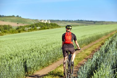 Genç bisikletçi alanın parça Bisiklete binme sırt çantası ile arkadan görünüş.