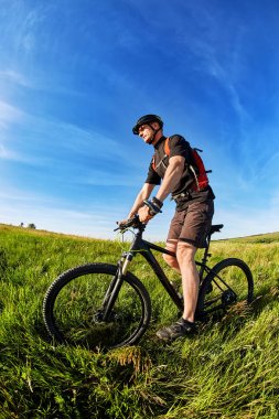 Genç bisikletçi mavi gökyüzü bir zemin üzerine yeşil çayır kask içinde.