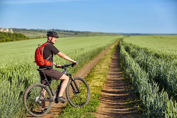 Atraktivní cyklista stojící horské kolo v poli s modrou oblohou na pozadí. — Stock fotografie