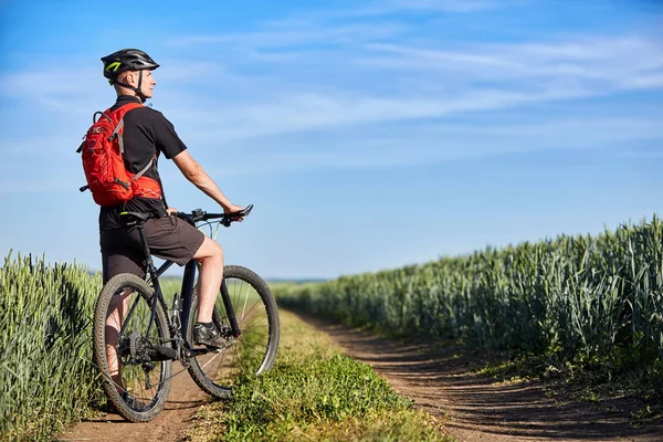 Attractive cyclist standing with mountain bicycle in field with blue sky on a background.