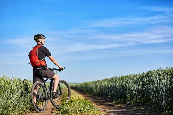 Atrakcyjne rowerzysta stoi z rowerem górskim w polu niebieski niebo na tle. — Zdjęcie stockowe