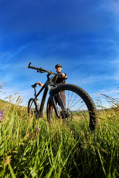 Молодий велосипедист в шоломі на зеленому лузі на фоні з блакитним небом . — стокове фото
