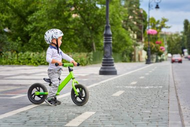 Child boy in white helmet riding on his first bike with a helmet. Bike without pedals. clipart