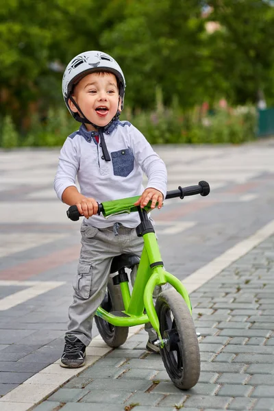Child boy in white helmet riding on his first bike with a helmet. Bike without pedals.
