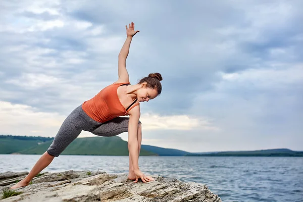 Junge Frau in Yoga-Pose auf dem großen Stein in der Nähe des schönen Flusses. — Stockfoto