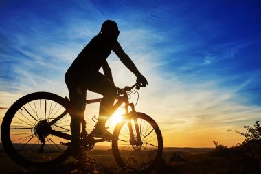 Bir bisikletçi ile gökyüzü arka plan güzel günbatımı üzerinde bisikletle silüeti.