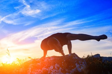 Çekici bir adam gecenin gündoğumu karşı kayaya yoga yaparken.