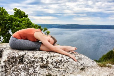Genç kadının güzel nehir üzerinde bir kayanın üzerinde karmaşık yoga egzersiz yapması.