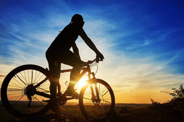 Silhueta de um ciclista com uma bicicleta no fundo do céu em belo pôr do sol . — Fotografia de Stock