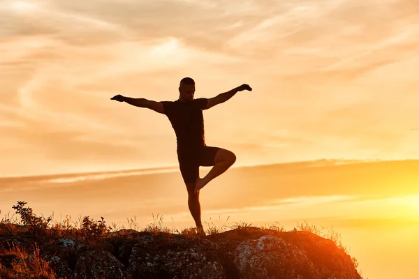 Silueta del hombre practicando yoga en la colina contra el hermoso atardecer . — Foto de Stock
