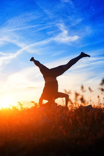 Jovem praticando ioga e alongamento em uma rocha ao pôr do sol . — Fotografia de Stock