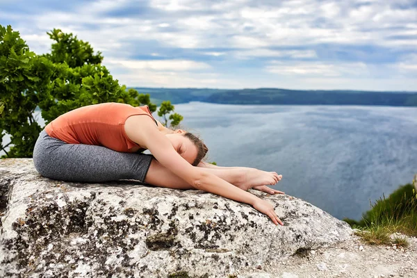 Genç kadının güzel nehir üzerinde bir kayanın üzerinde karmaşık yoga egzersiz yapması. — Stok fotoğraf