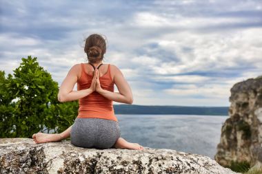 Yoga poz rock nehir üzerinde oturan genç kadın arkadan görünüş.