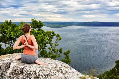 Yoga poz rock nehir üzerinde oturan genç kadın arkadan görünüş.