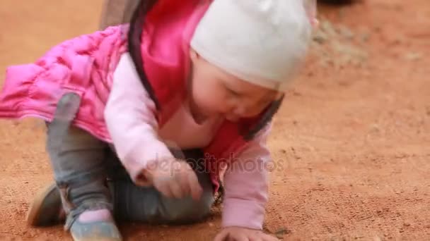 Симпатична маленька дівчинка, одягнена в рожевий одяг, сидить на дитячому майданчику на відкритому повітрі . — стокове відео