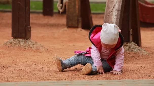 Schattig klein babymeisje gekleed in het roze kleding, zittend op de speelplaats in de openlucht. — Stockvideo