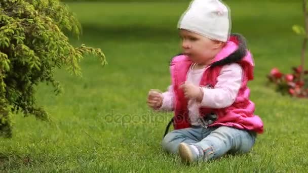 Linda niña sonriente arrastrándose sobre una hierba verde en el parque de la ciudad . — Vídeo de stock