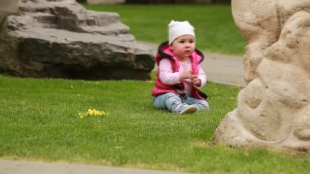 Linda niña sonriente arrastrándose sobre una hierba verde en el parque de la ciudad . — Vídeos de Stock