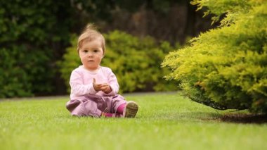 Bush yakınındaki bir yeşil çayır üzerinde oturan güzel mutlu küçük kız bebek.