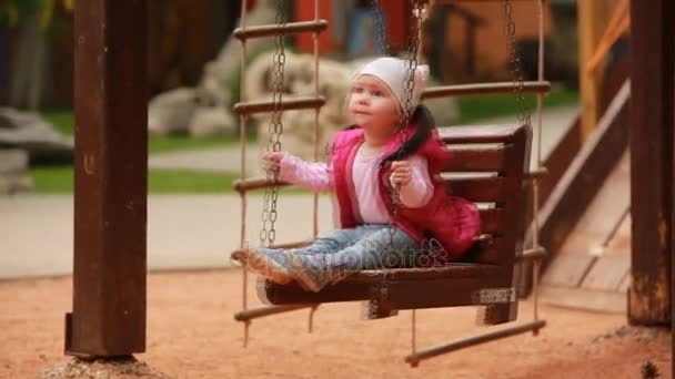 Schattig babymeisje genieten van een schommel rijden op een speelplaats in het stadspark. — Stockvideo