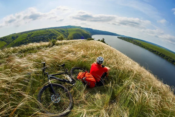 Giovane ciclista appoggiato sul prato sul riverbero in montagna con mountain bike contro il bel cielo . — Foto Stock