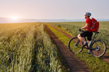 Genç bisikletçi dağ bisikletçi gündoğumu karşı kırsal alanında yol ile.