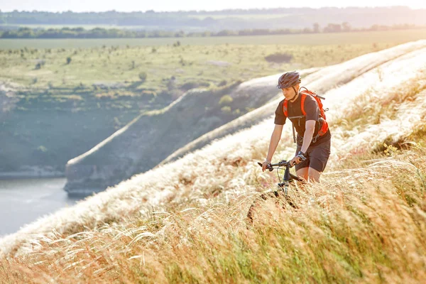 Atraktivní cyklista rirding horské kolo nad krásnou řekou v poli na venkově. — Stock fotografie