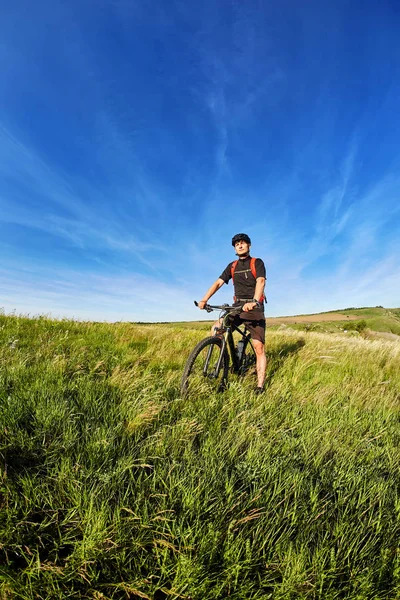 田舎の雲と青空が広がってに対して緑の牧草地の若いサイクリスト. — ストック写真